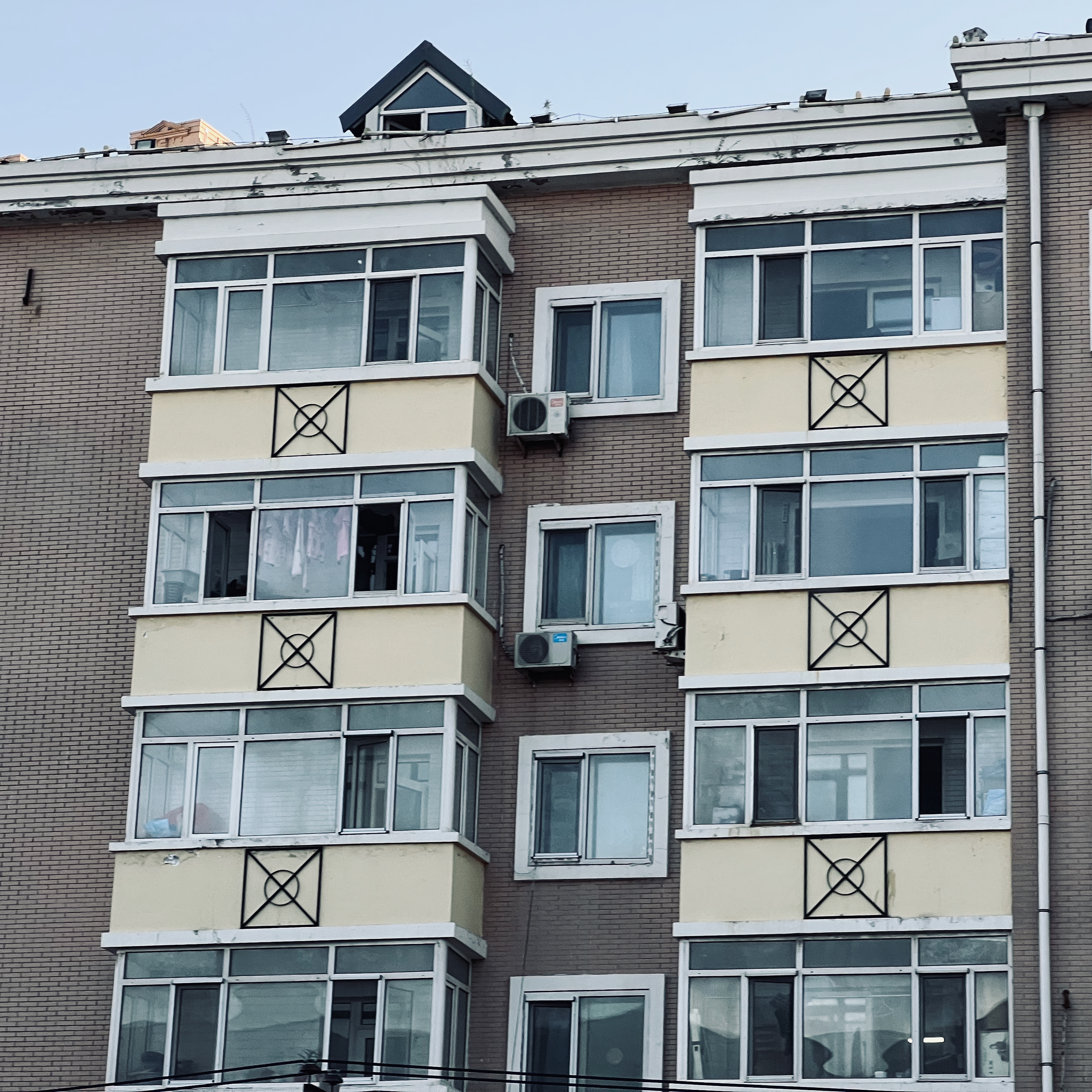 A photo of the outside of an apartment building, having a vertical slice jutting out with three walls of windows on it.