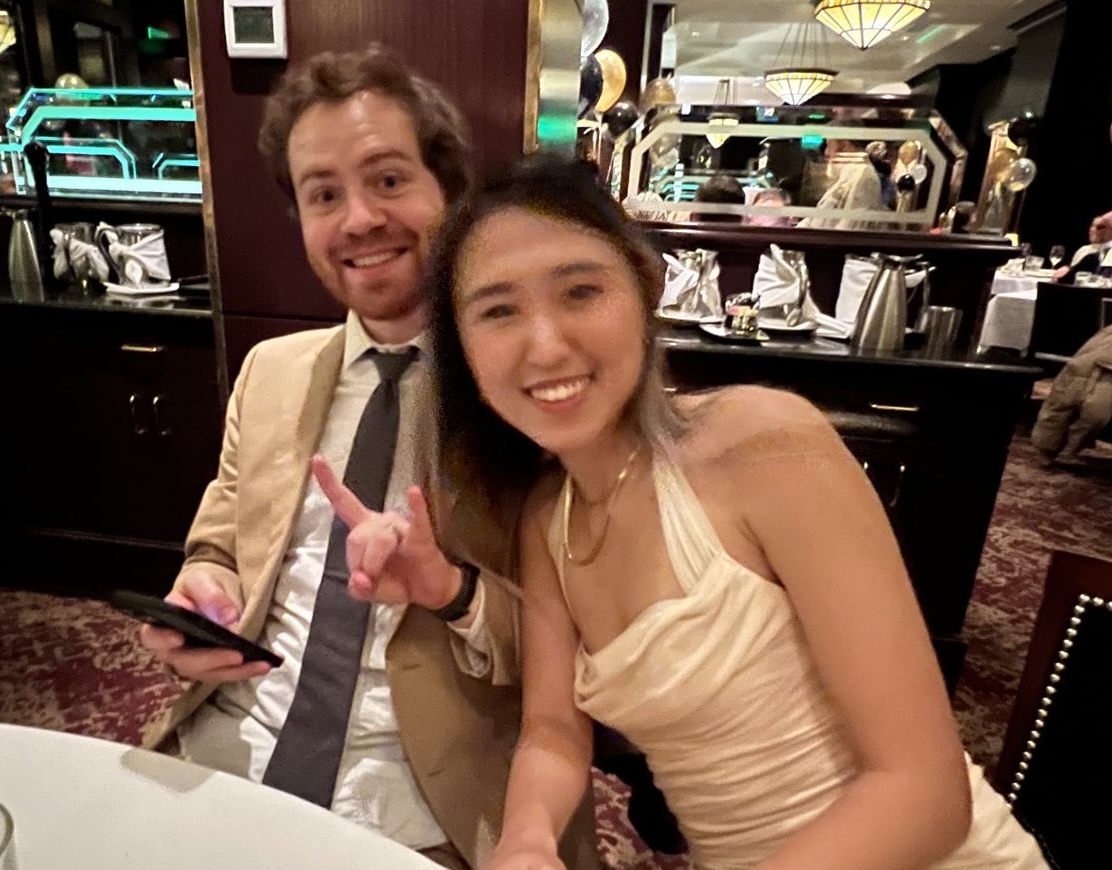A photo of me and Summer dressed up at a nice dinner. I am white. Summer is Chinese. We are both laughing and I am showing the 'sign of the horns'.