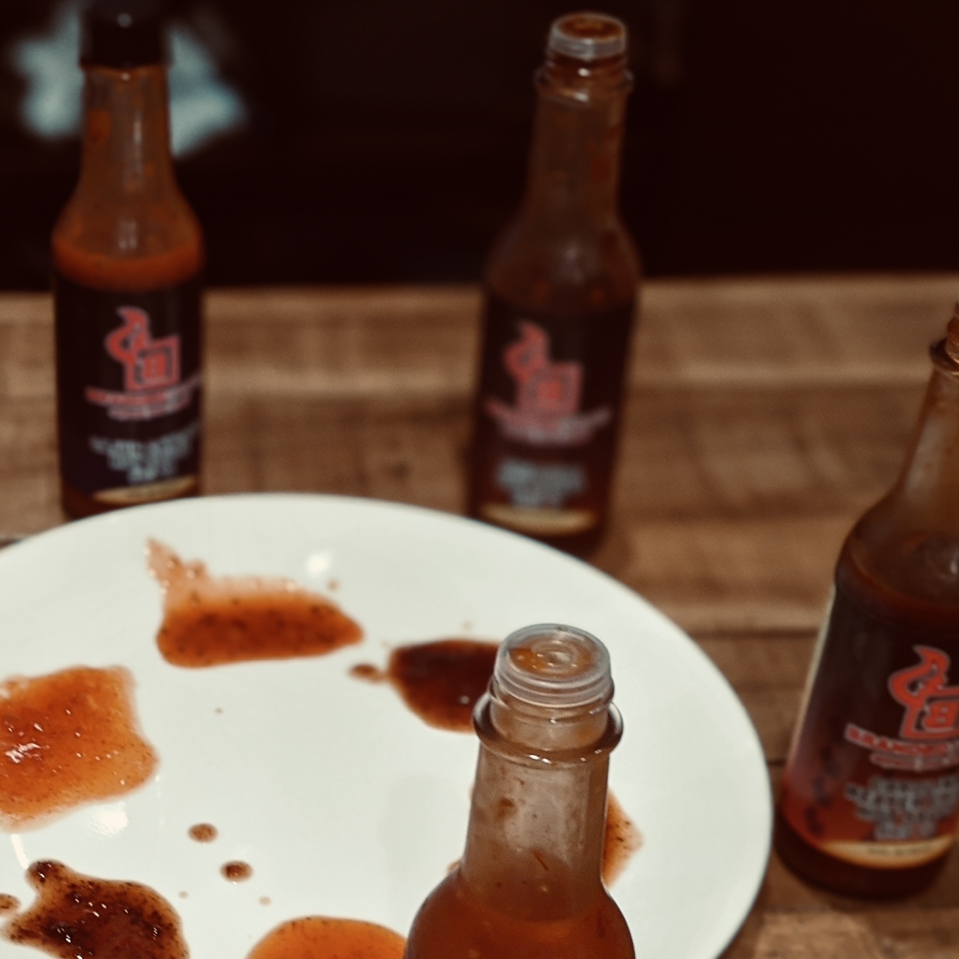 Several hot sauce bottles around a plate, with part of each bottle poured into a spot on the plate that allows for dipping